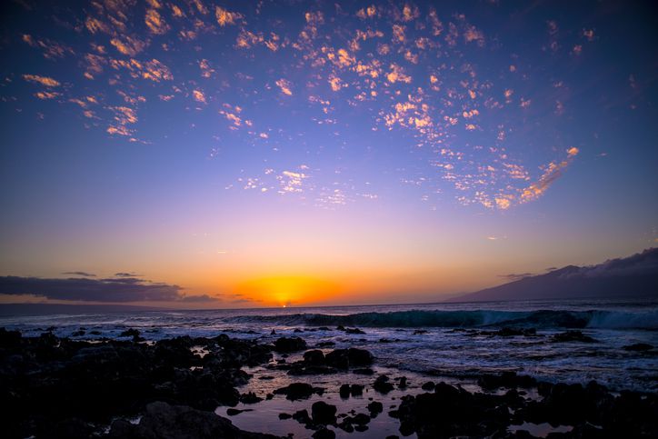 <p>Taken from the shores of Maui, the sun sets over the rocky shores of Lanai. Near Shipwreck Beach, this oceanfront portion of the island is ideal for exploring poiawa, the reddish-brown earth, and rock formations, covering Lanai. </p>