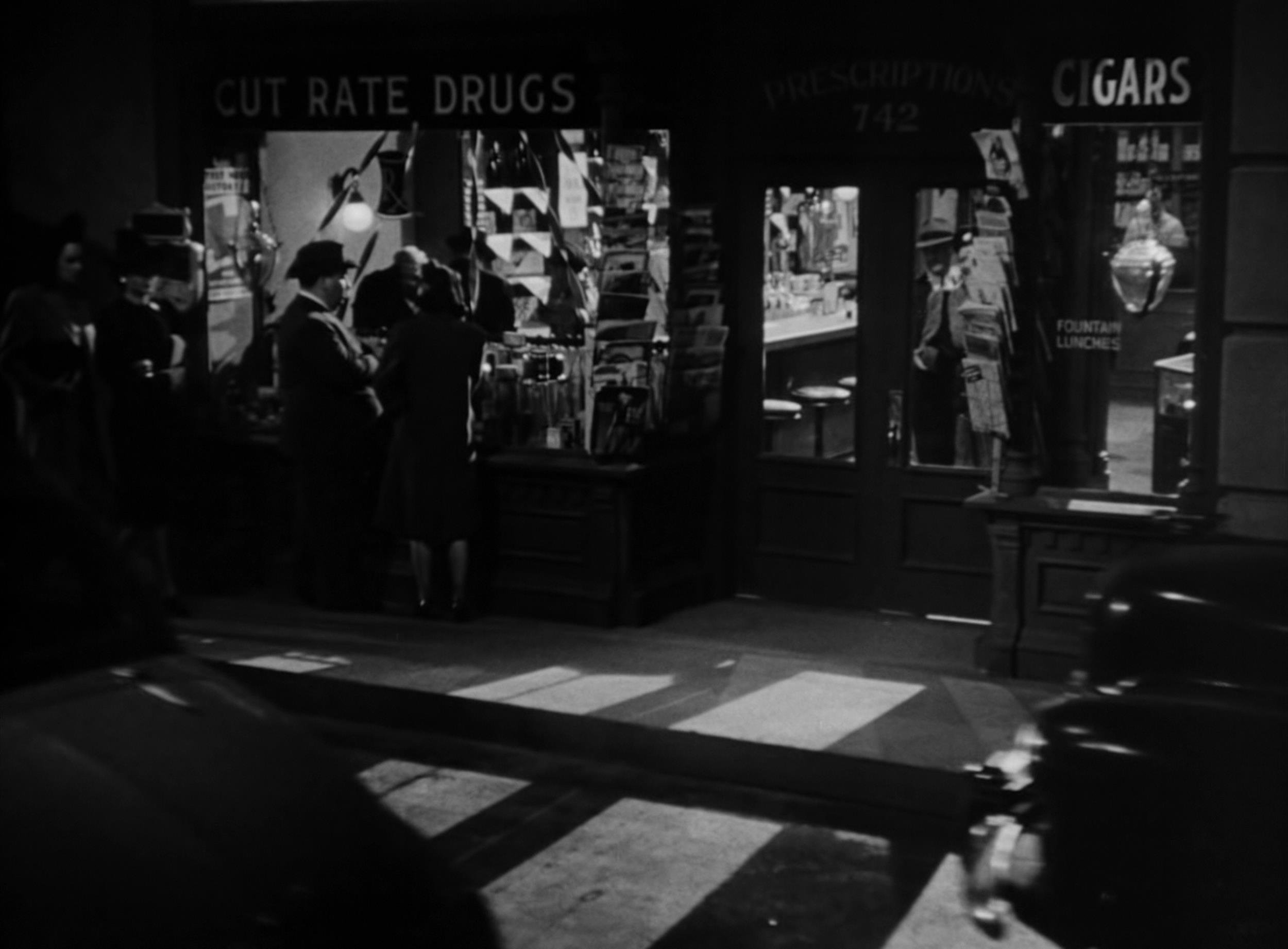 <p>Why would somebody shop at a store called “Cut Rate Drugs.” Maybe that’s what Hitchcock’s character is talking about in his cameo. He and a female extra stand in front of a store window of the aforementioned store, but they are in the distance and can’t be overheard.</p>