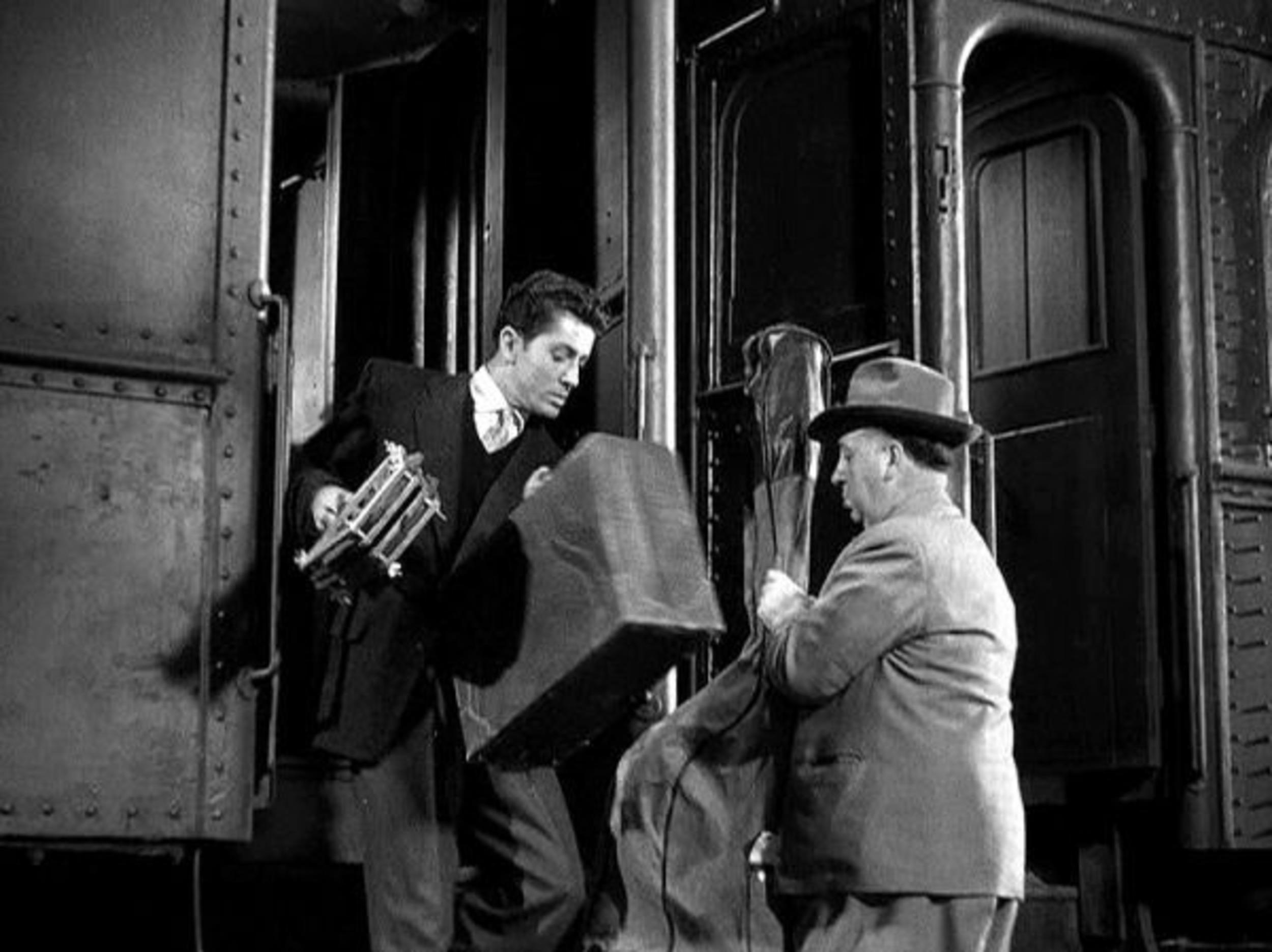<p>You’ll never guess where Hitchcock has his cameo. Yep, it’s on the train. Or, rather, getting onto the train. The guy seemed to enjoy playing men carrying instruments with him. This time, it seems like he’s trying to board the train carrying a cello, or perhaps even a double bass.</p>