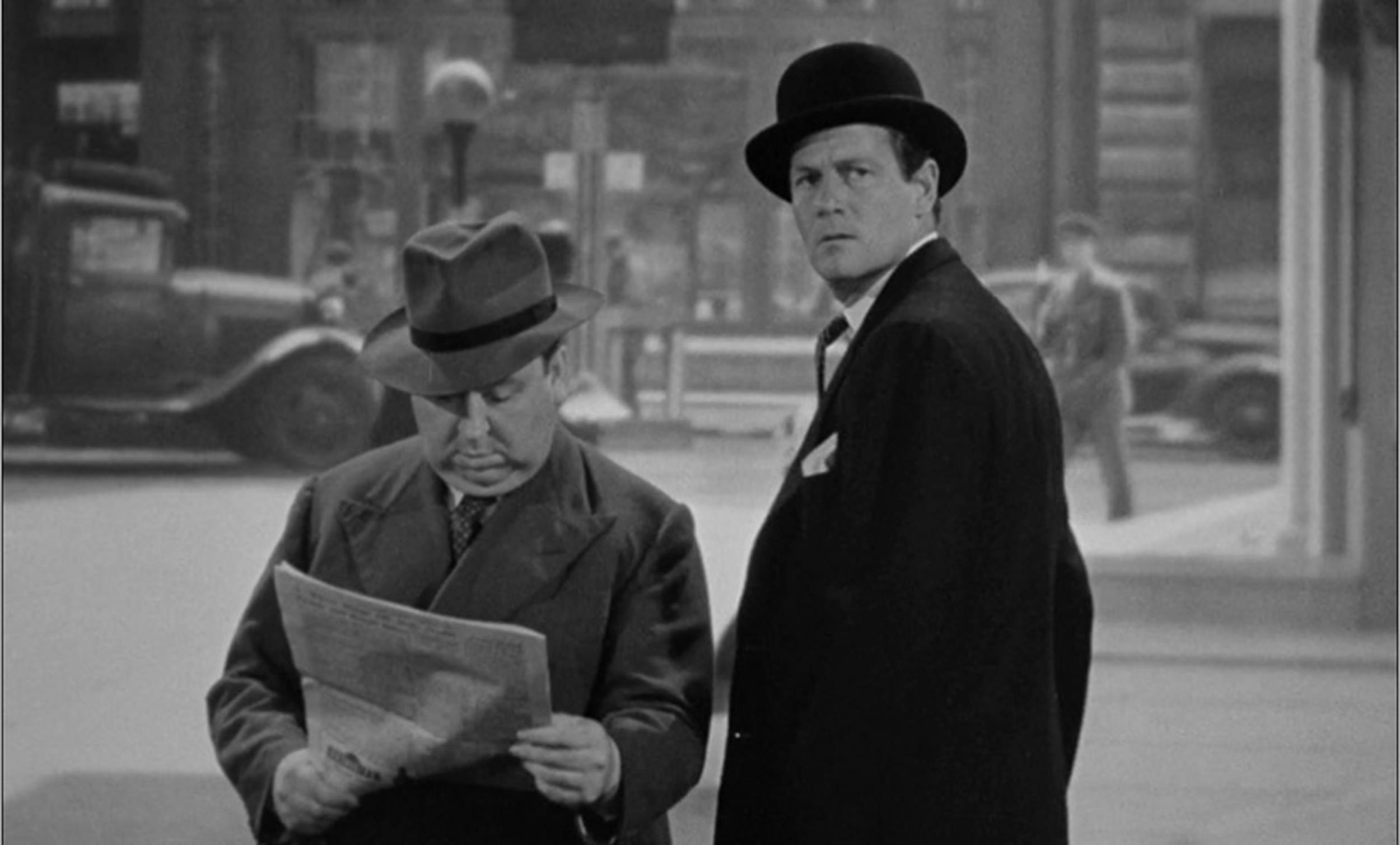 <p>Star Joel McRea is walking one way down the street, and here comes Hitchcock walking the other way. Now in America, Hitch has set aside the bowler hat he often wore in his British films for a more robust hat. As he walks he’s reading a newspaper which seems dangerous, especially in a Hitchcock film.</p>
