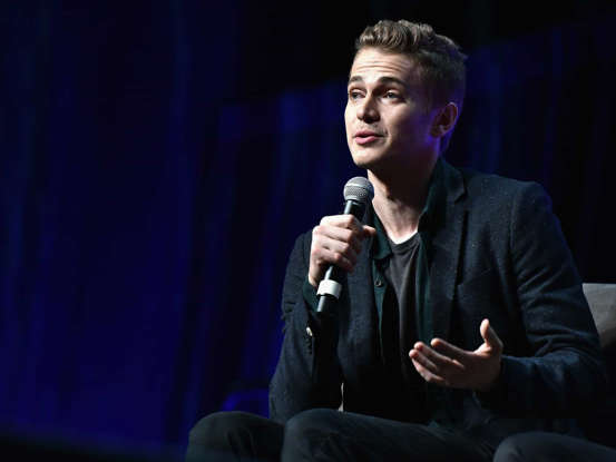 Hayden Christensen wearing a suit and tie talking on a stage