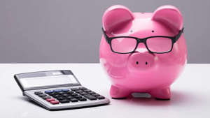 a close up of a teddy bear sitting on a table: edit Close-up Of A Piggybank With Eyeglasses And Calculator On Desk