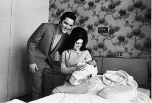 Elvis Presley, Priscilla Presley sitting on a bed: Lisa Marie Presley poses for her first picture on Feb. 5, 1968, with her proud parents, Elvis and Priscilla Presley.