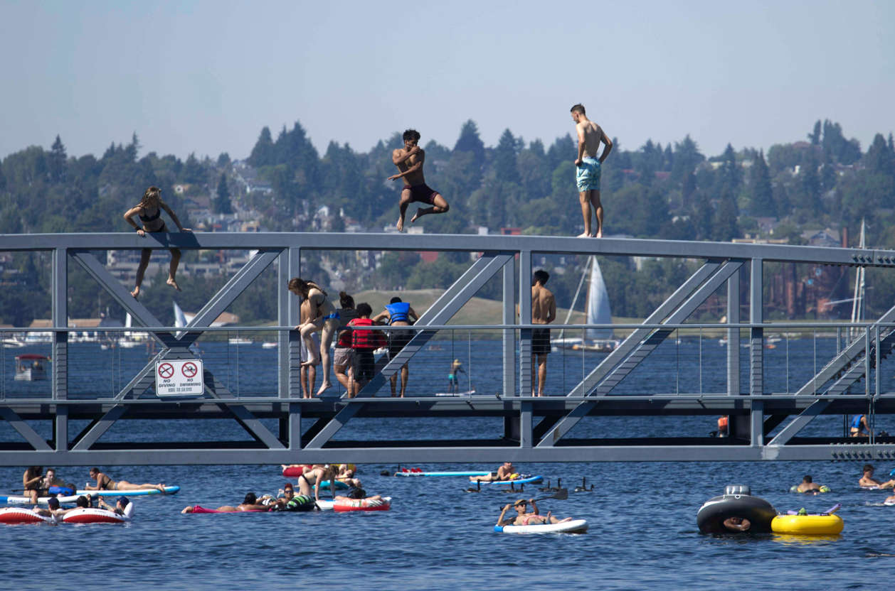 Slide 13 of 27: Two people jump from a pedestrian bridge at Lake Union Park into the water during a heat wave hitting the Pacific Northwest, Sunday, June 27, 2021, in Seattle. A day earlier, a record high was set for the day with more record highs expected today and Monday.