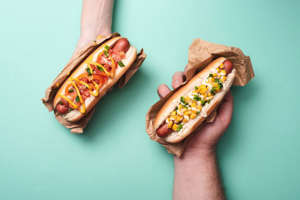 a person holding a hot dog: Turns out people have strong opinions about hot dogs. If you’re from a city that’s known for its hot dogs, chances are you’re loyal to a very specific set of toppings. Have you ever tried putting ketchup on your hot dog in Chicago? We don’t recommend it! Because so many cities have their own version of the ideal dog, we put together this list of famous hot dogs around the U.S. in cities like Atlanta, Chicago, Detroit and more.