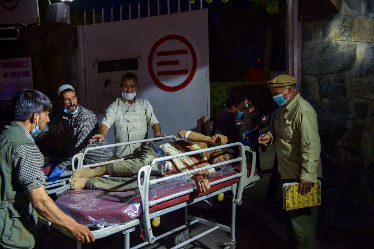 Slide 4 of 8: Medical and hospital staff bring an injured man on a stretcher for treatment after two powerful explosions, which killed at least six people, outside the airport in Kabul on August 26, 2021.