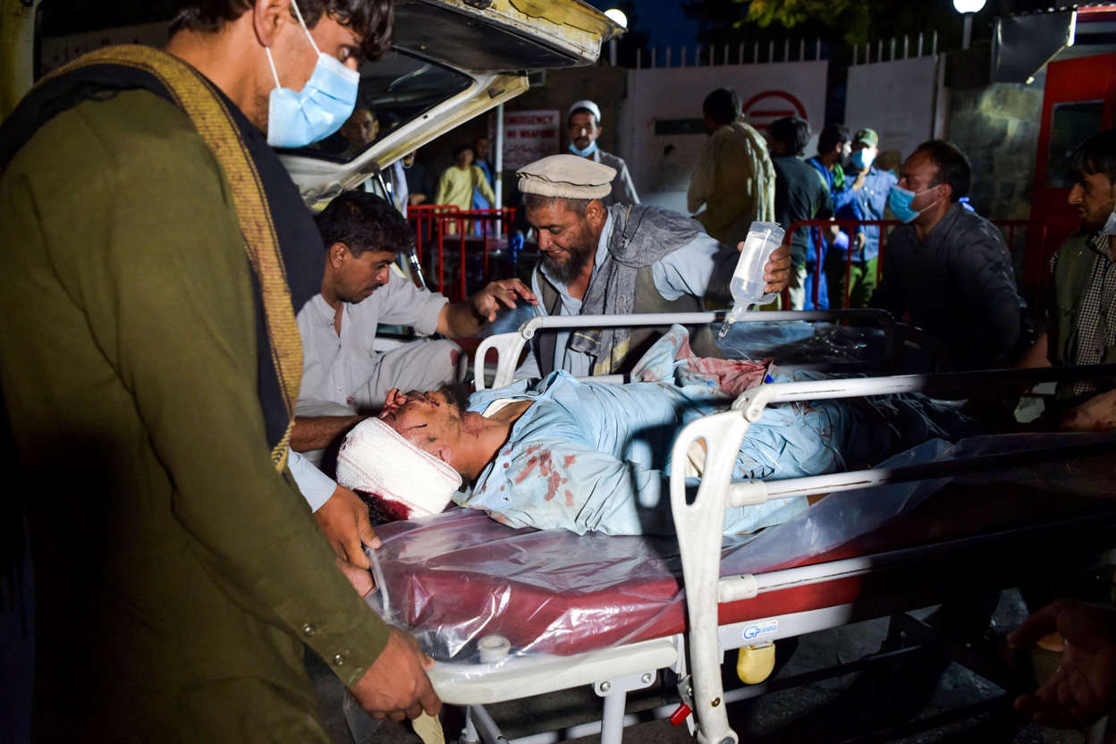 Slide 5 of 8: Medical and hospital staff bring an injured man on a stretcher for treatment after two blasts outside the airport in Kabul on August 26, 2021.