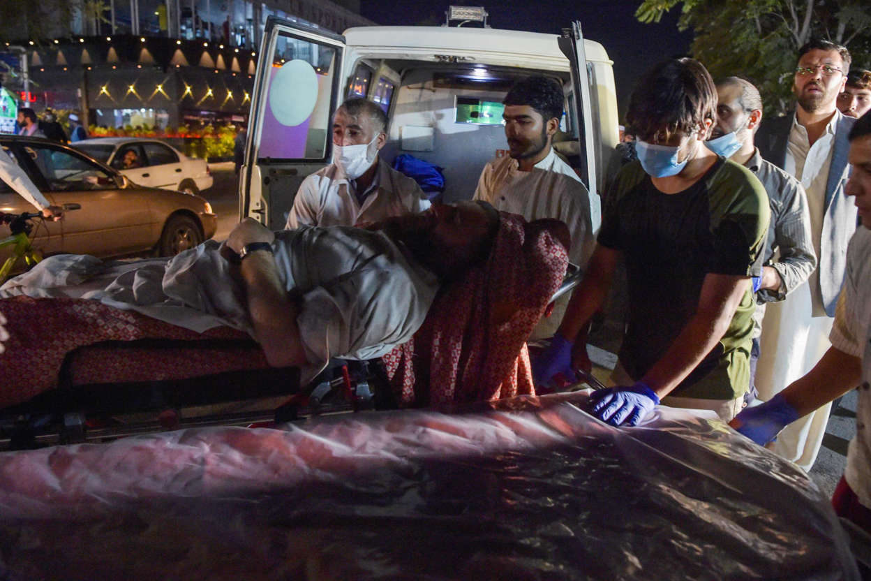 Slide 6 of 8: Volunteers and medical staff bring an injured man for treatment after two powerful explosions outside the airport in Kabul on Aug/ 26, 2021.