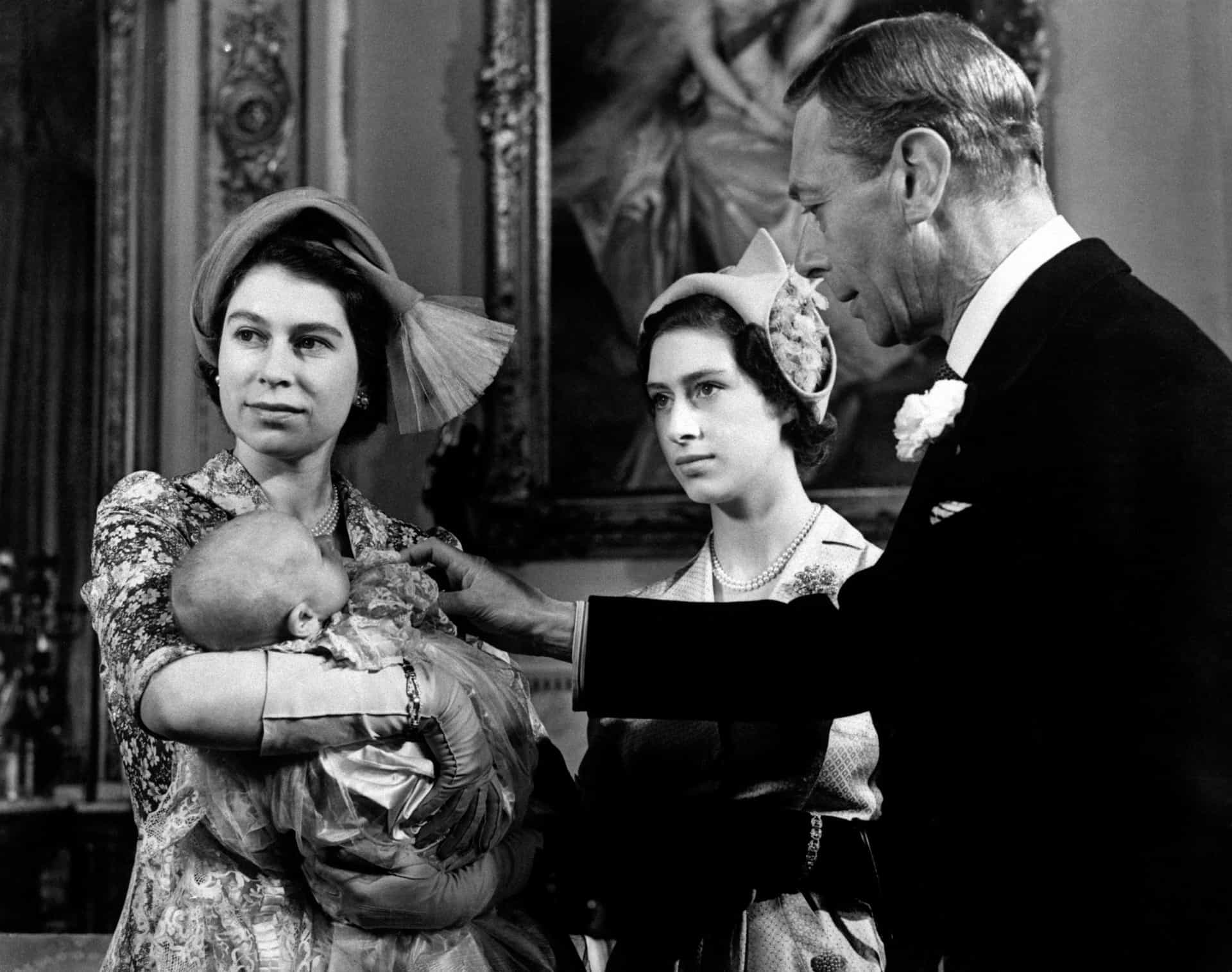 Elisabeth wiegt ihr zweites Kind, Prinzessin Anne, nach der Taufe des Babys im Buckingham Palace im Jahr 1950. Tante Prinzessin Margaret und Großvater König Georg VI. schauen zu.
