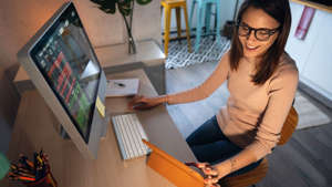 a woman sitting at a table using a laptop computer: High-angle view of a young woman trading cryptocurrency on a computer and digital tablet stock photo