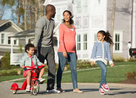 Couple walking through suburban neighborhood with youngest child riding a tricycle.