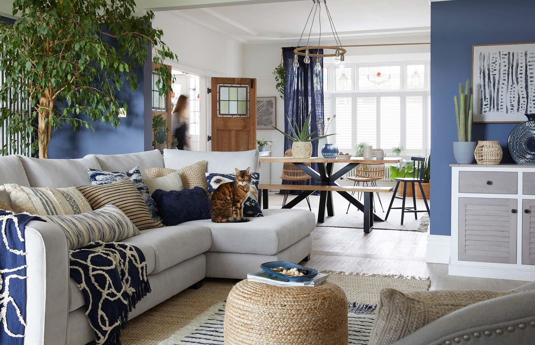 Create a cohesive look in a large, multiuse space by embracing a unifying theme. Here, a subtle coastal scheme works hard to tie together the living room and dining area. Deep blue walls and furnishings create a visual connection and draw the eye through the adjacent spaces, while jute and rattan accessories complete the harmonious feel.