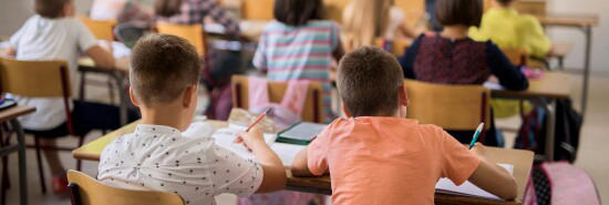 Back view of school children learning in the classroom. Focus in on foreground.