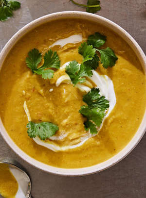 golden yellow mulligatawny soup garnished with yogurt and cilantro in a white bowl