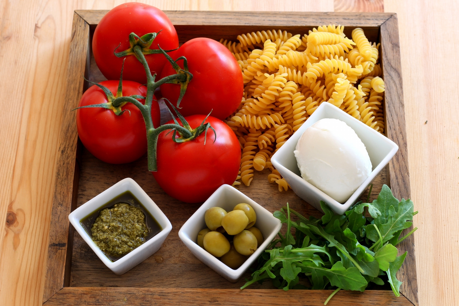 Slide 2 de 14: Para 4 pessoas:  6 tomates maduros Sal 1 dente de alho 4 colheres de sopa de azeite de oliva 4 colheres de chá de orégano 2 grandes punhados de azeitonas verdes 4 colheres de chá de pesto 250 g mozzarella fresca (vaca ou búfala, de acordo com o gosto) 400 g de macarrão (fusilli, penne ou rigatoni) 2 grandes punhados de rúcula (para finalizar) 