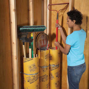 woman places a garden rake into a cardboard concrete tube in the garage