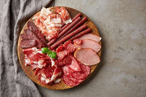 Cold smoked meat plate with prosciutto, salami, bacon, pork chops, cheese and olives on gray stone background. From top view