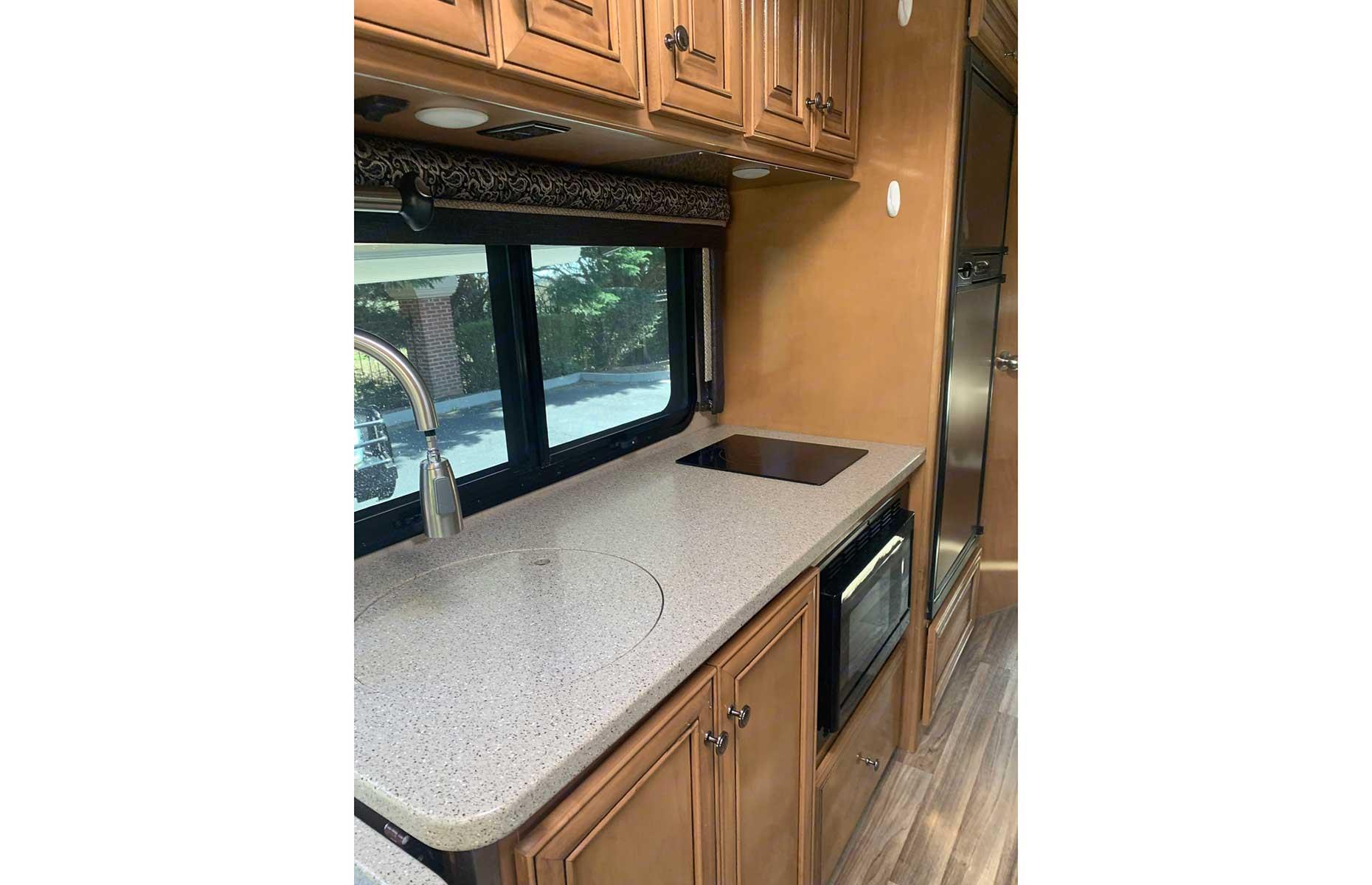Inside includes gray, marble-like countertops and wooden cupboards with a booth-like dinette and TV. The kitchen includes a sink, induction stove, microwave and refrigerator/freezer. There’s a cabin above the driver’s seat which sleeps two and a queen size bed at the rear of the vehicle, where one of the TVs is located. Fresh linen and blankets are included in the price.