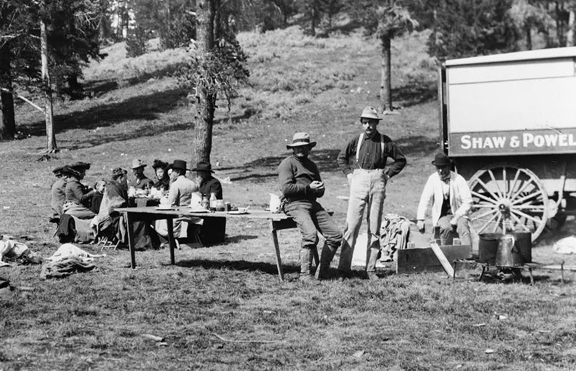 In the park's earliest decades, private automobiles were prohibited too. Instead, tourists explored the park in their own horse-drawn wagons or on stagecoach tours led by guides. Here a group of travelers and guides picnic beside their vehicle, in a clearing at the edge of a forest.