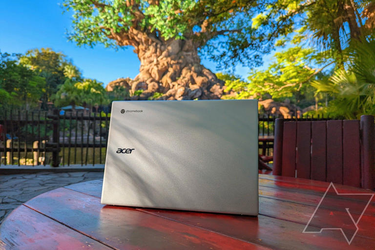 An Acer Chromebook 514 (CB514-2H/T) on a wooden table on a stone patio next to a pond with greenery around it