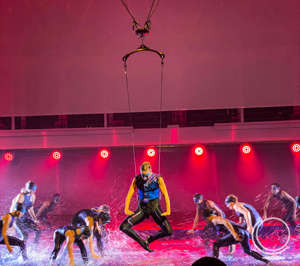 Performers dancing in water in aqua theater while aerial performer is hanging on a harness. 