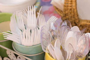 Plastic White Forks and Clear Spoons in Decorative Serving Tray Holders, Exterior, Afternoon Sunlight, Medium Shot, High Angle, Serving Items in Background in Soft Focus.