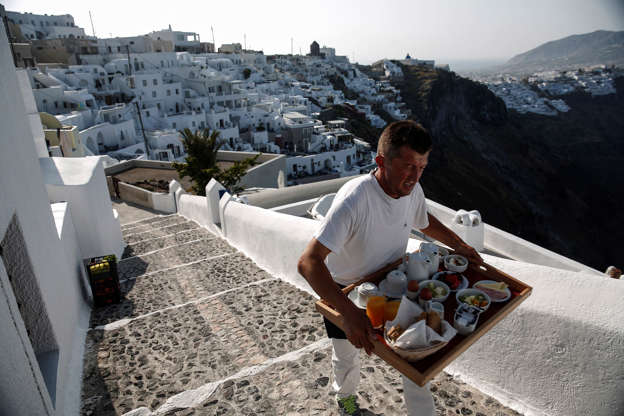 ÎÎ¹Î±ÏÎ¬Î½ÎµÎ¹Î± 13 Î±ÏÏ 42: A hotel worker delivers a breakfast tray up a cobbled stairway in the town of Fira on the island of Santorini, Greece, on Wednesday, May 20, 2015. German Chancellor Angela Merkel said that greater efforts are needed to unlock bailout funds for Greece after late-night negotiations with Greek Prime Minister Alexis Tsipras failed to yield any sign of a breakthrough.