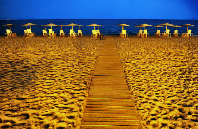 ÎÎ¹Î±ÏÎ¬Î½ÎµÎ¹Î± 42 Î±ÏÏ 42: Bloomberg's Best Photos 2013: Straw parasols stand above empty tables and chairs in evening light on a beach in Asprovalta, Greece, on Sunday, July 21, 2013. For Prime Minister Antonis Samaras, the tangible signs of Greece's recovery are the tourists pouring into Athens from cruise ships and airplanes.