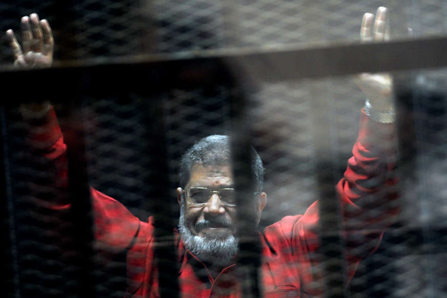 FILE - In this June 21, 2015 file photo, former Egyptian President Mohammed Morsi, wearing a red jumpsuit that designates he has been sentenced to death, raises his hands inside a defendants cage in a makeshift courtroom at the national police academy, in an eastern suburb of Cairo, Egypt.