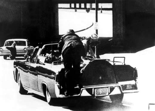 Slide 4 of 25: JOHN F KENNEDY - 1963 A member of the Secret Service stands on the bumper of the presidential limousine in Dallas, seconds after President John F. Kennedy was shot. The President is in the back seat to the left, Mrs. Kennedy is standing up in the back seat to the right.