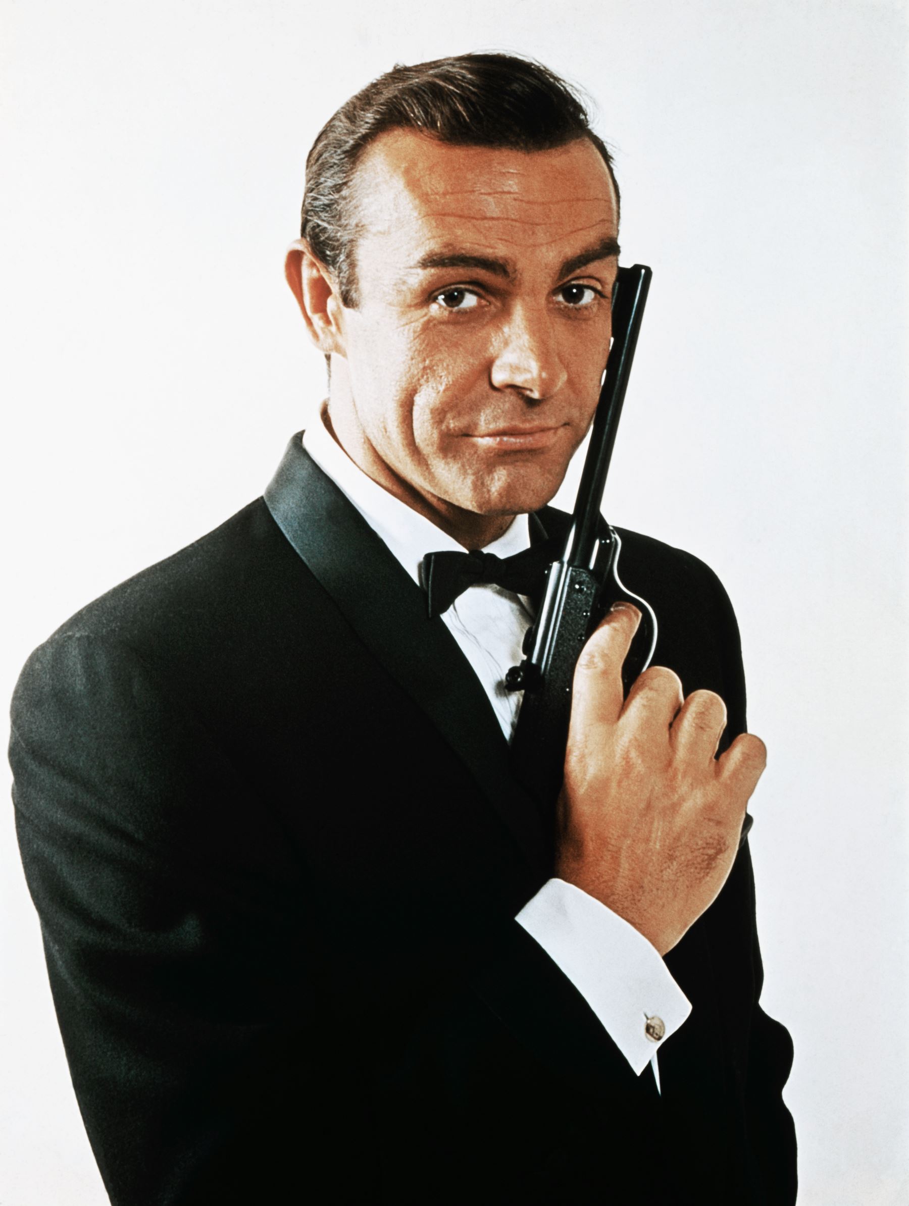 ÎÎ¹Î±ÏÎ¬Î½ÎµÎ¹Î± 29 Î±ÏÏ 45: (Original Caption) Waist-up portrait of Sean Connery, as James Bond, caressing the barrel of a gun against the side of his face. Connery is wearing a tuxedo and bow tie and smiling slightly.