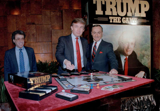 Diapositiva 2 de 14: Real estate mogul Donald Trump, left, takes his turn as George Ditomassi, president of the Milton Bradley company, looks on at a news conference in New York, announcing a new board game, "Trump, The Game," Feb. 7, 1989. The game allows players to bid against each other and make deals for big ticket real estate. Man at far left is unidentified. (AP Photo/Mario Suriani)