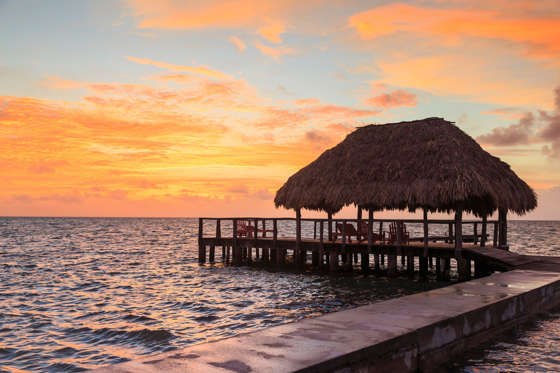 Stilted waterfront pier and thatched roof at sunset, St. Georges Caye, Belize, Central America.
