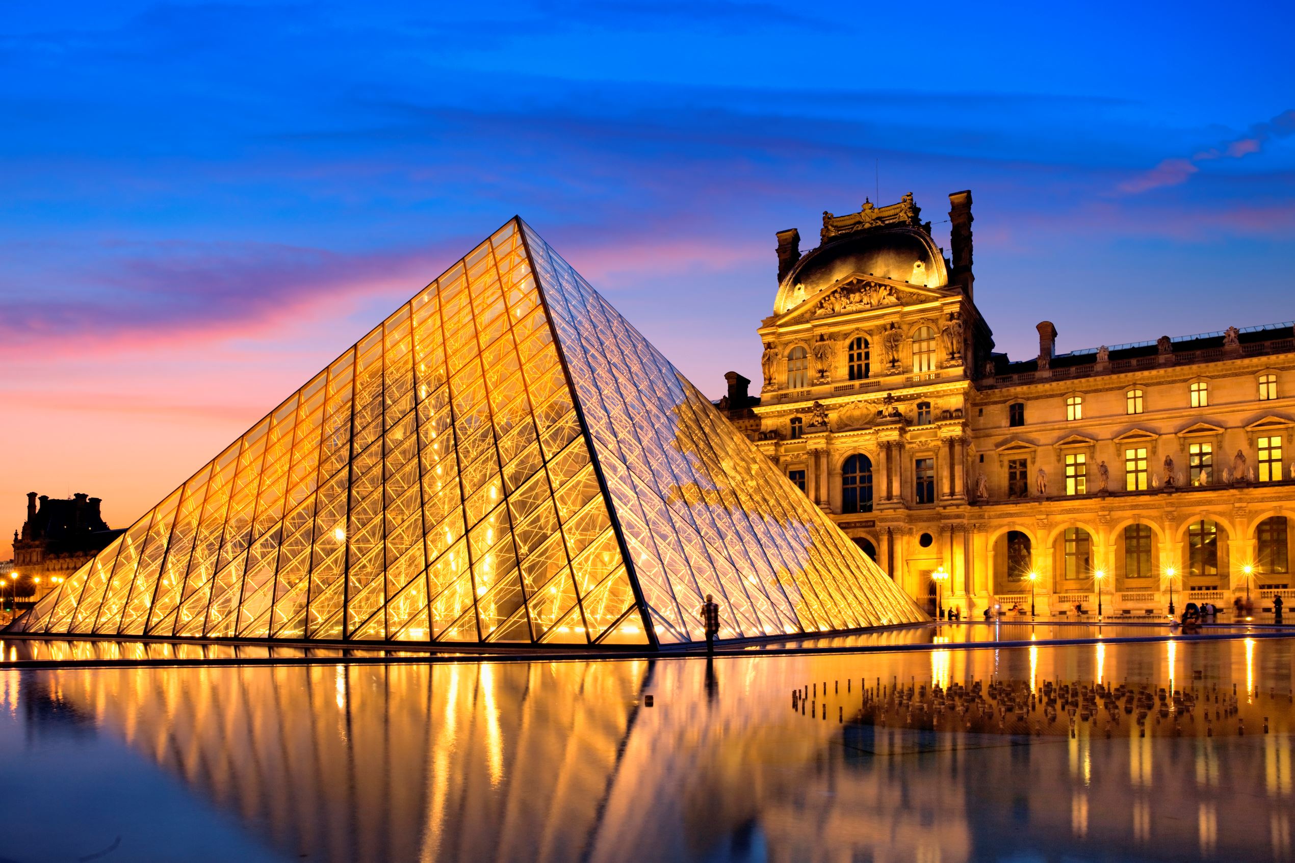 Slide 2 of 9: The Louvre Museum illuminated glass pyramid entrance.