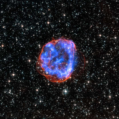 Slide 77 of 86: In this image, an expanding shell of debris called SNR 0519-69.0 is left behind after a massive star exploded in the Large Magellanic Cloud, a satellite galaxy to the Milky Way. Multimillion degree gas is seen in X-rays from Chandra, in blue. The outer edge of the explosion (red) and stars in the field of view are seen in visible light from the Hubble Space Telescope.
