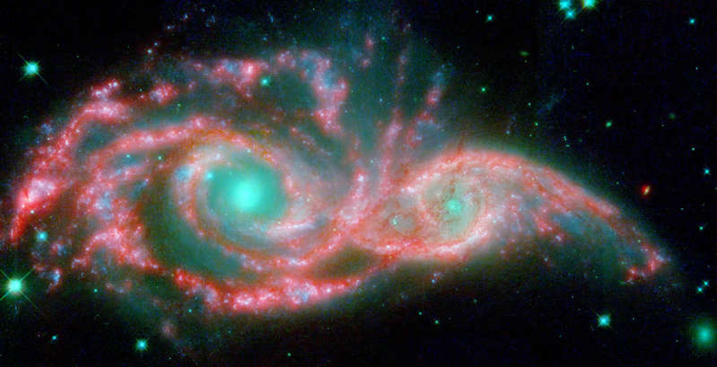 Slide 13 of 81: These shape-shifting galaxies have taken on the form of a giant mask. The icy blue eyes are actually the cores of two merging galaxies, called NGC 2207 and IC 2163, and the mask is their spiral arms. The false-color image consists of infrared data from NASA's Spitzer Space Telescope (red) and visible data from NASA's Hubble Space Telescope (blue/green).  NGC 2207 and IC 2163 met and began a sort of gravitational tango about 40 million years ago. The two galaxies are tugging at each other, stimulating new stars to form. Eventually, this cosmic ball will come to an end, when the galaxies meld into one. The dancing duo is located 140 million light-years away in the Canis Major constellation.  Image Credit: NASA/JPL-Caltech/STScI/Vassar