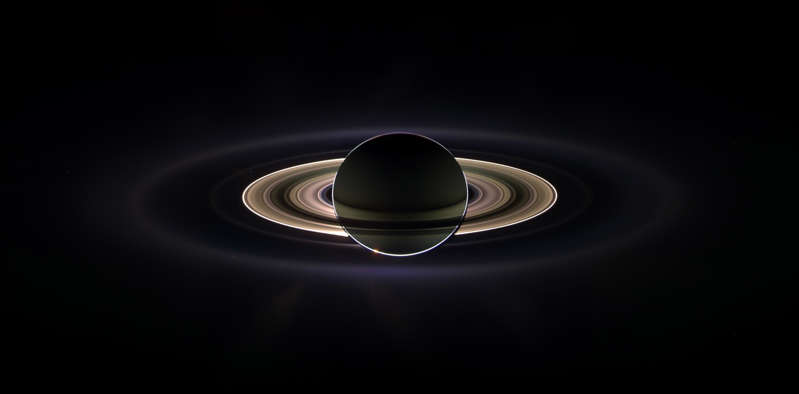 Slide 44 of 86: With giant Saturn hanging in the blackness and sheltering Cassini from the sun's blinding glare, the spacecraft viewed the rings as never before.  This marvelous panoramic view was created by combining a 165 images taken by the Cassini wide-angle camera over nearly three hours on Sept. 15, 2006. The mosaic images were acquired as the spacecraft drifted in the darkness of Saturn's shadow for about 12 hours, allowing a multitude of unique observations of the microscopic particles that comprise Saturn's faint rings.  The narrowly confined G ring is easily seen here, outside the bright main rings. Encircling the entire system is the much more extended E ring. The icy plumes of Enceladus, whose eruptions supply the E ring particles, betray the moon's position in the E ring's left side edge.  Interior to the G ring and above the brighter main rings is the pale dot of Earth. Cassini views its point of origin from close to a billion miles away in the icy depths of the outer solar system.  Image Credit: NASA/JPL/Space Science Institute
