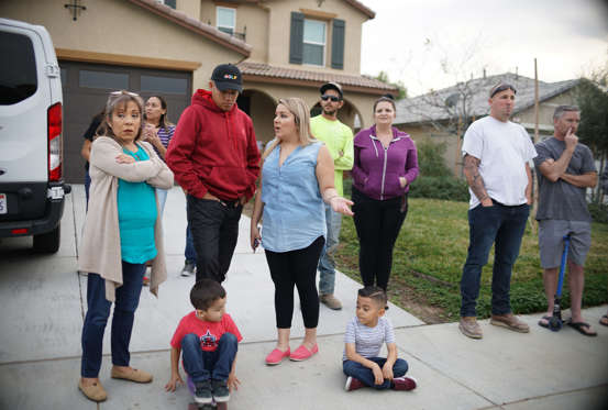 Slide 4 of 8: Neighbors stand outside a home (not pictured) where a couple was arrested after police discovered that 13 people had been held captive in filthy conditions with some shackled to beds with chains and padlocks, January 15, 2018 in Perris California.