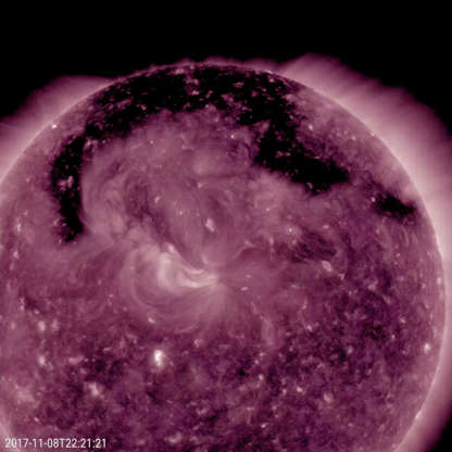 Slide 8 of 86: A broad hole in the corona was the Sun's dominant feature November 7-9, 2017, as shown in this image from NASA's Solar Dynamics Observatory. The hole is easily recognizable as the dark expanse across the top of the Sun and extending down in each side. Coronal holes are magnetically open areas on the Sun that allow high-speed solar wind to gush out into space. They always appear darker in extreme ultraviolet. This one was likely the source of bright aurora that shimmered for numerous observers, with some reaching down even to Nebraska.