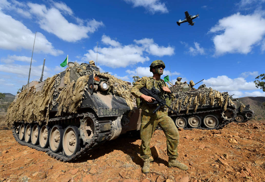Slide 33 of 51: TOWNSVILLE, AUSTRALIA - OCTOBER 21: Sapper Nick Denis of the Australian Army looks on after a live fire attck in front of a M113 APC (Amoured Personnel Carrier) as a RAAF (Royal Australian Air Force) PC-9 aircraft flies overhead during the 3rd Brigade Live Fire Exercise 'Brolga Run' on October 21, 2016 in Townsville, Australia. Exercise Brolga Run is the 3rd Brigade's major training activity for the year. (Photo by Ian Hitchcock/Getty Images)