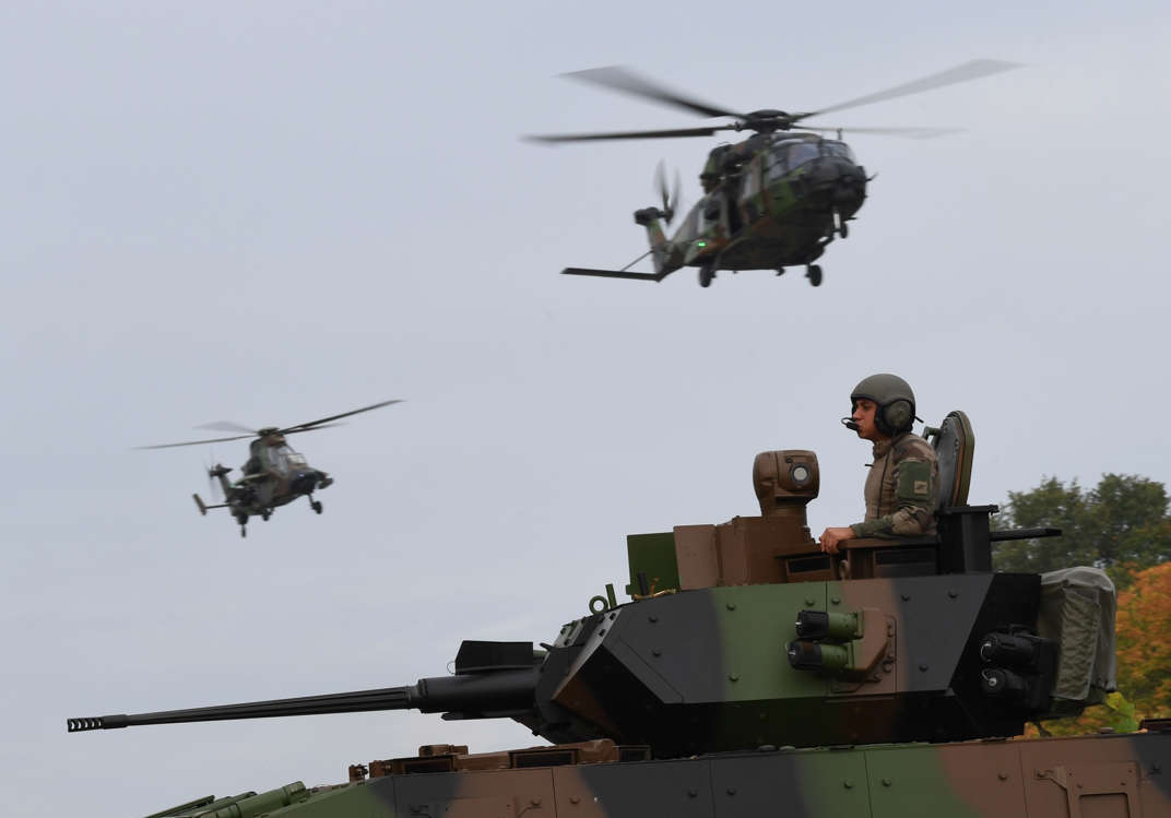 Slide 45 of 51: A soldier stands atop a VBCI armored combat vehicle, as a tactical transport NH90 'Caiman' military helicopter (Top R) and a Tiger attack helicopter fly over, during a presentation drill to the French Institute of Advanced Studies in National Defence (Institut des hautes Etudes de Defense Nationale) of the means of the French army ground force on October 19, 2017 in Versailles-Satory. / AFP PHOTO / Eric FEFERBERG (Photo credit should read ERIC FEFERBERG/AFP/Getty Images)