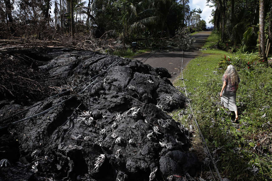 Slide 4 of 119: Hannique Ruder, a 65-year-old resident living in the Leilani Estates subdivision, walks past the mound of hardened lava while surveying the neighborhood Friday, May 11, 2018, near Pahoa, Hawaii. Kilauea has destroyed more than 35 structures since it began releasing lava from vents about 25 miles (40 kilometers) east of the summit crater. (AP Photo/Jae C. Hong)