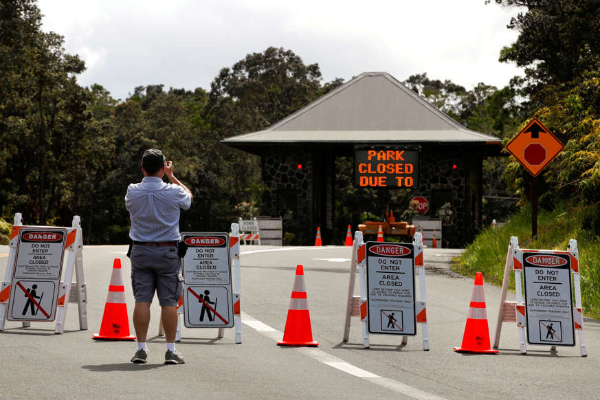 Slide 3 of 119: Ken Gadd, a first-time visitor from Dayton, Ohio, takes pictures of the entrance to Volcanoes National Park, Hawaii, Friday, May 11, 2018. The park is closed due to the threat of an explosive volcanic eruption. Warnings that Hawaii's Kilauea volcano could shoot boulders and ash out of its summit crater are prompting people to rethink their plans to visit the Big Island. (AP Photo/Jae C. Hong)