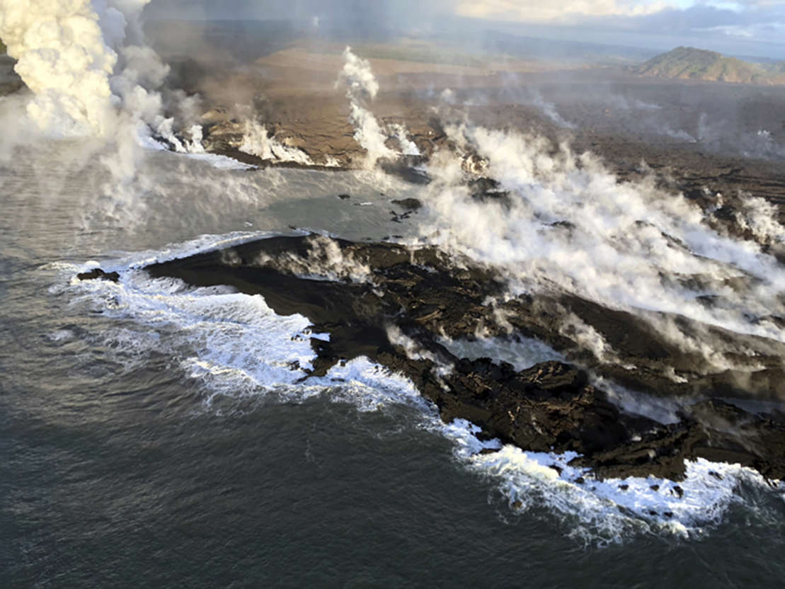 Slide 1 of 100: This photo provided by the U.S. Geological Survey shows new land formed by lava from KIlauea Volcano where the bay and village of Kapoho once stood on the island of Hawaii Wednesday, June 13, 2018. The new coastline, following the ragged lava-ocean interface, is approximately 2.1 kilometers (1.3 miles) in length. The white steamy laze plume marks the location of the most active lava entry site.