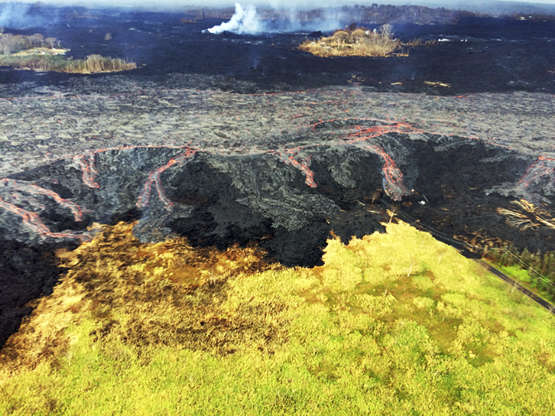 Slide 10 of 100: In this Sunday, June 10, 2018 photo provided by the U.S. Geological Survey, overflows of the Kilauea Volcano's upper fissure 8 lava channel flowing laterally sent small flows of lava down the "levee" walls, middle, near Kapoho on the island of Hawaii. See two-lane road and power lines at lower right for scale. These overflows did not extend far from the channel, so they posed no immediate threat to nearby areas. (U.S. Geological Survey via AP)