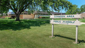 a green and white street sign sitting on the grass: Oshkosh Area School District Administration Office, 215 S. Eagle St.