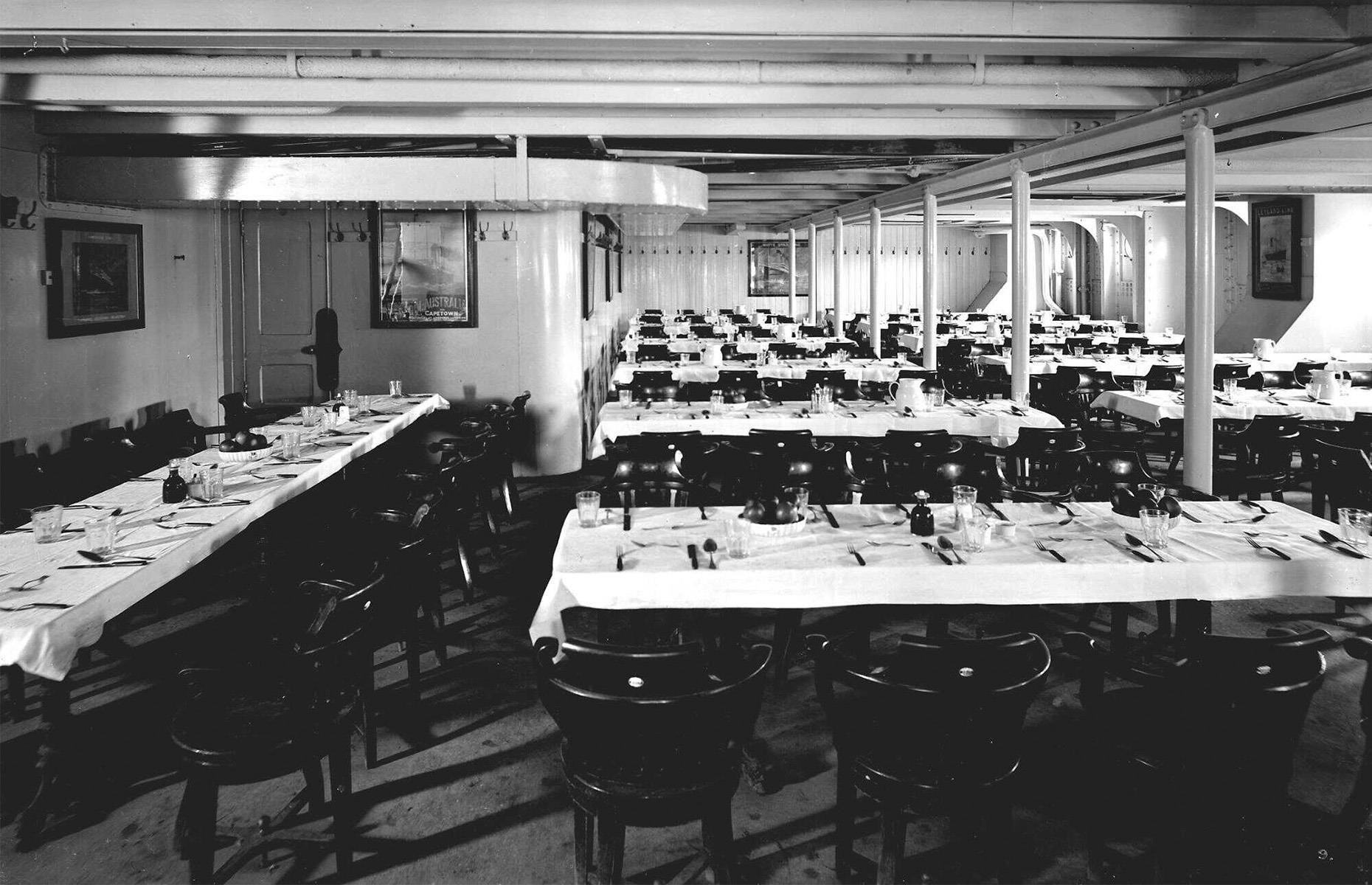 The food and dining rooms were plain in comparison to the first- and second-class experience, but were still a great improvement for steerage passengers of the time, who usually had to bring their own food. The dining areas were painted white with bright side lighting, long communal wooden tables and chairs and enameled walls. Pictured is the third-class dining saloon (1911) on the RMS Olympic, the Titanic’s near-identical sister ship.