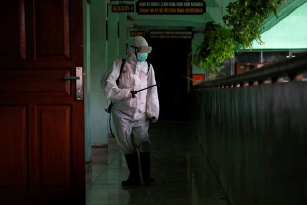 Slide 3 of 154: A volunteer from Indonesia's Red Cross sprays disinfectant at the corridor of a school closed amid the spread of coronavirus (COVID-19) in Jakarta, Indonesia, March 16, 2020. REUTERS/Willy Kurniawan