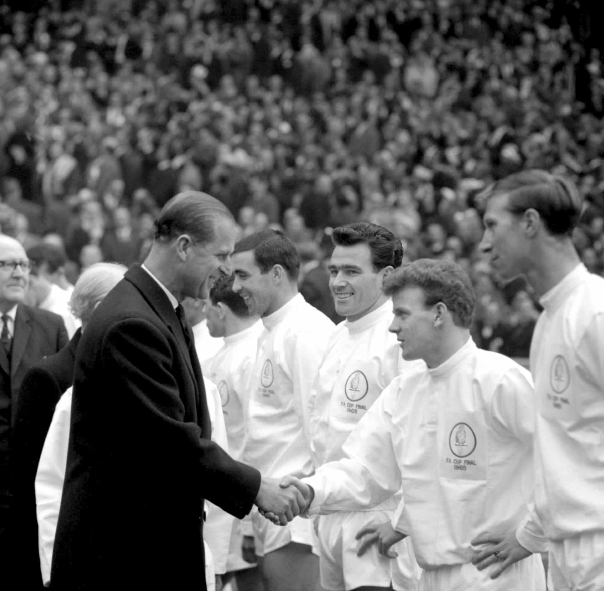 En un partido de fútbol en el norte de Inglaterra, dándole un choque de manos a jugadores del Leeds United como Jack Charlton, mientras Jim Storrie observa.