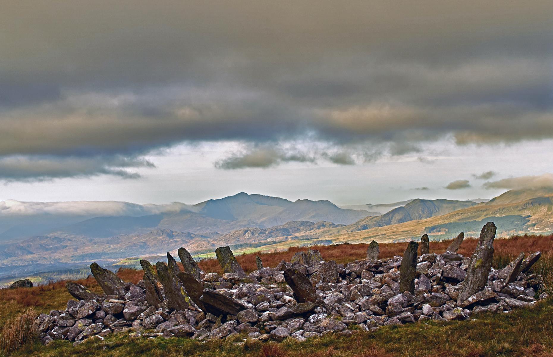Slide 18 of 31: The Bronze Age ring cairn of Bryn Cader Faner would once have marked a burial site. With its name translating as “the hill crowned with the throne of the flag jagged slate”, the spiky structure is an arresting sight amid a lonely patch of moorland in the brooding hills of Snowdonia. The 4,000-year-old formation has around 15 long, thin stone slabs of slate that lean outwards, reminiscent of a crown of thorns. Find more reasons to love Wales here.